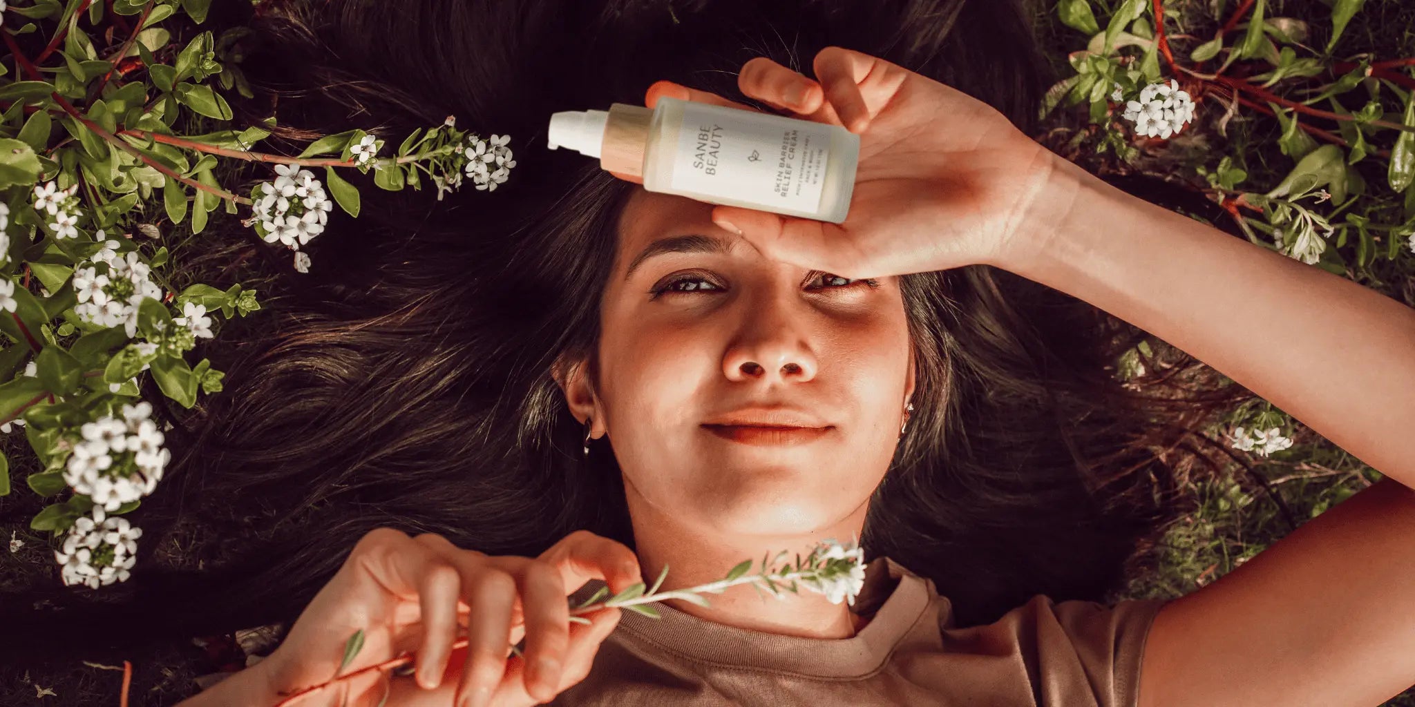 Female holding Sanbe skincare, laying in the grass