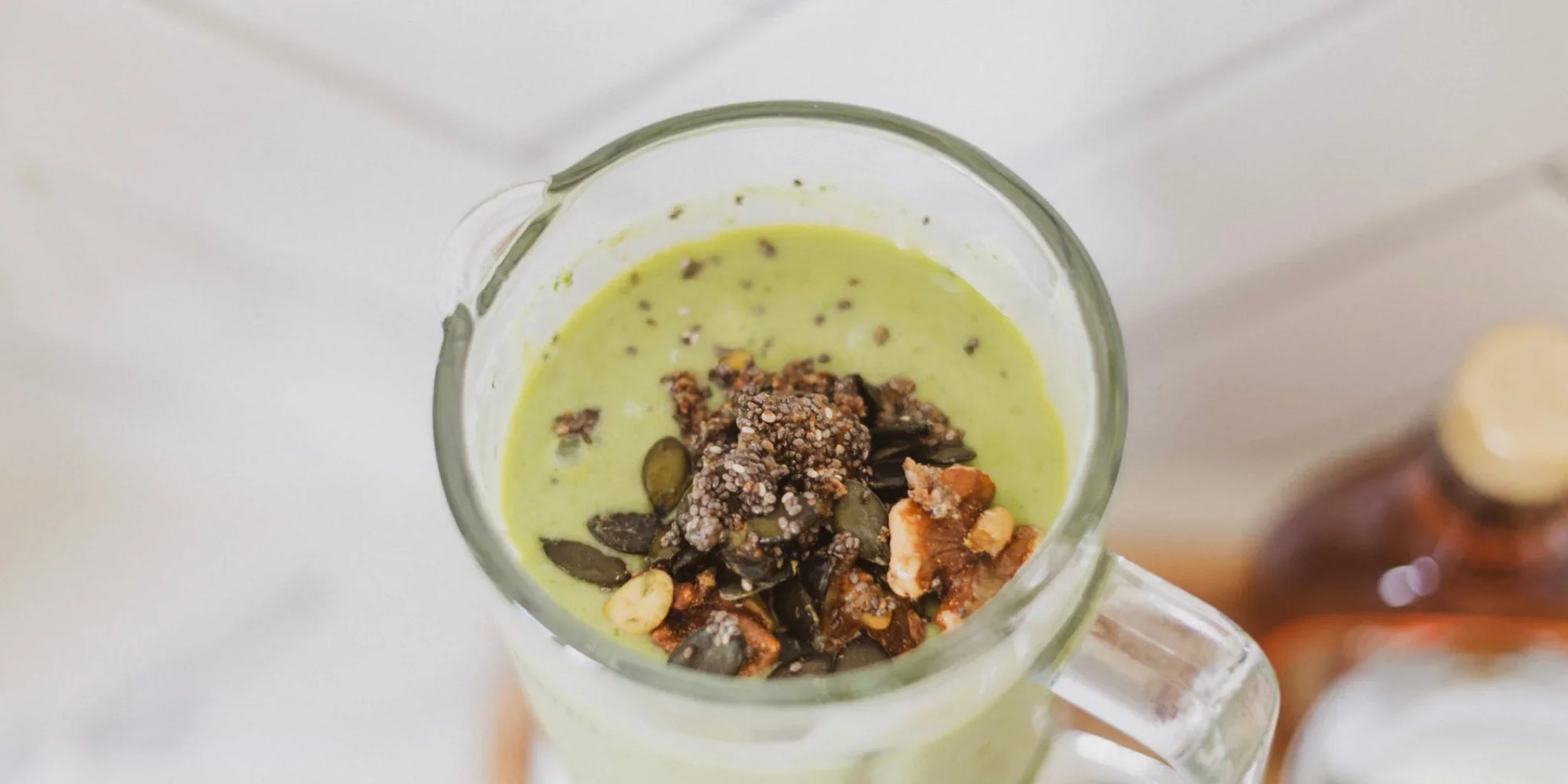 Green smoothie for skin in a glass mug topped with pumpkin seeds, chia seeds, and walnuts, morning light