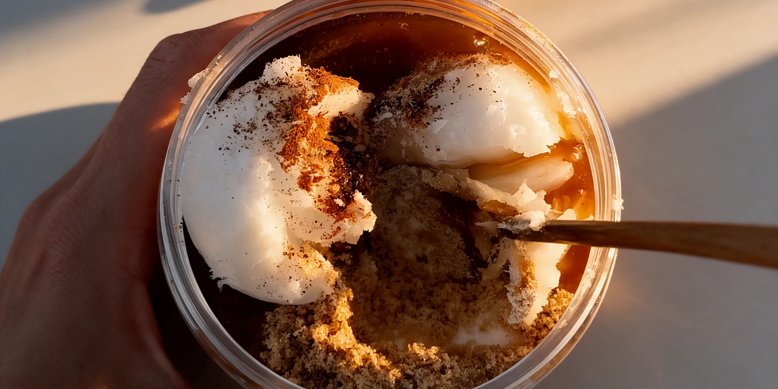 Hand holding a jar of apple pie sugar scrub with cinnamon and coconut oil.